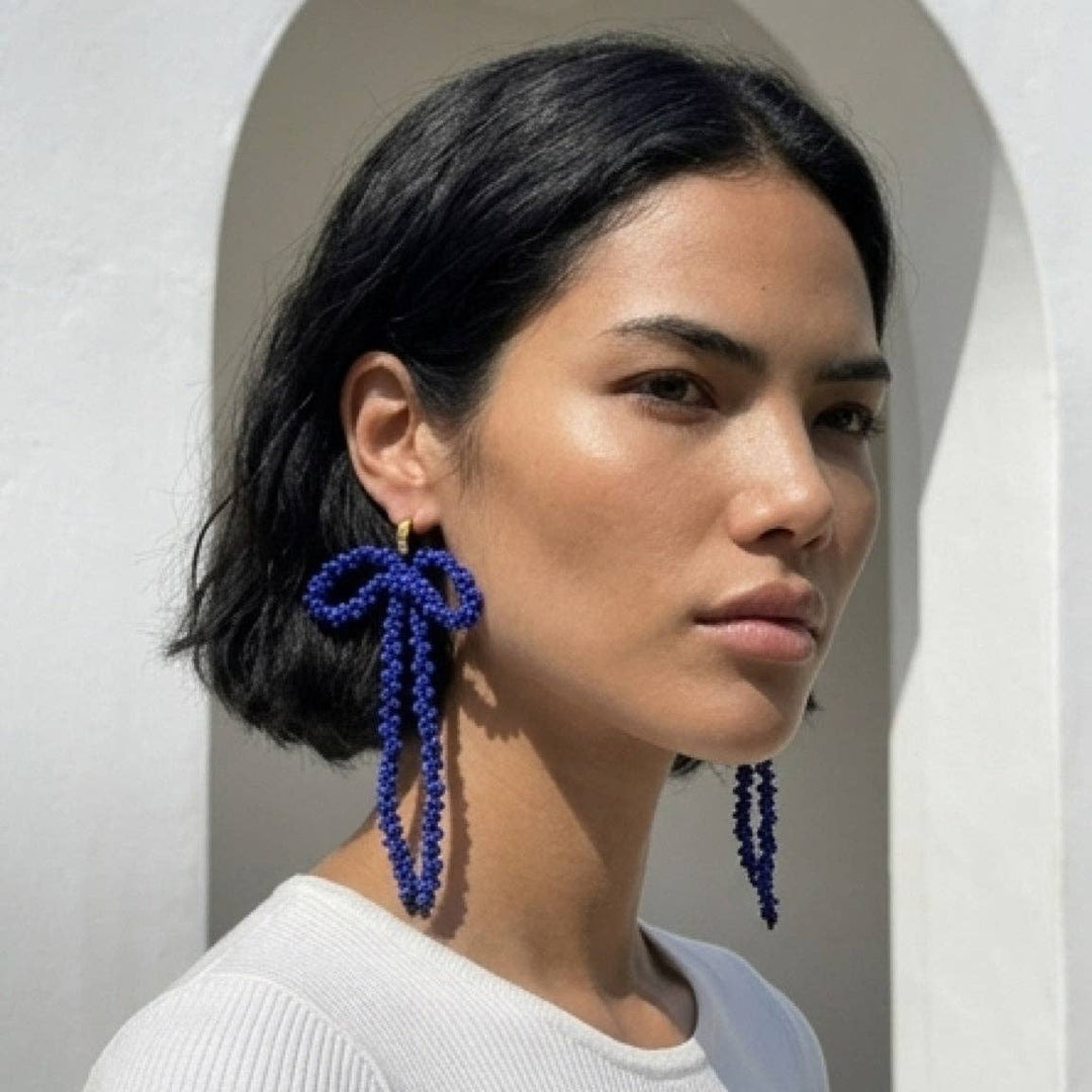 Woman wearing blue beaded bow-shaped earrings against a neutral background