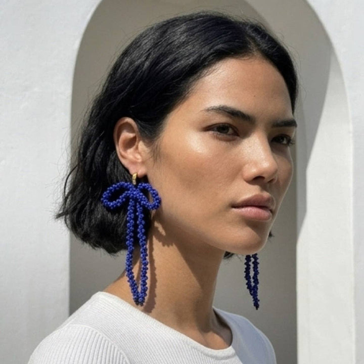 Woman wearing blue beaded bow-shaped earrings against a neutral background