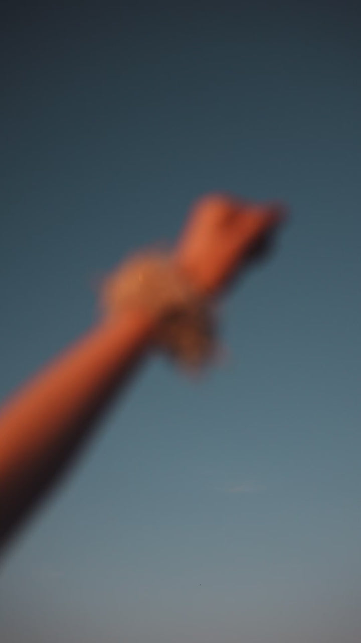 A video featuring someone's arm wearing a Lowland Summer scrunchie, twisting her wrist playfully, with the threads of the scrunchie fluttering in the breeze against a clear sky.